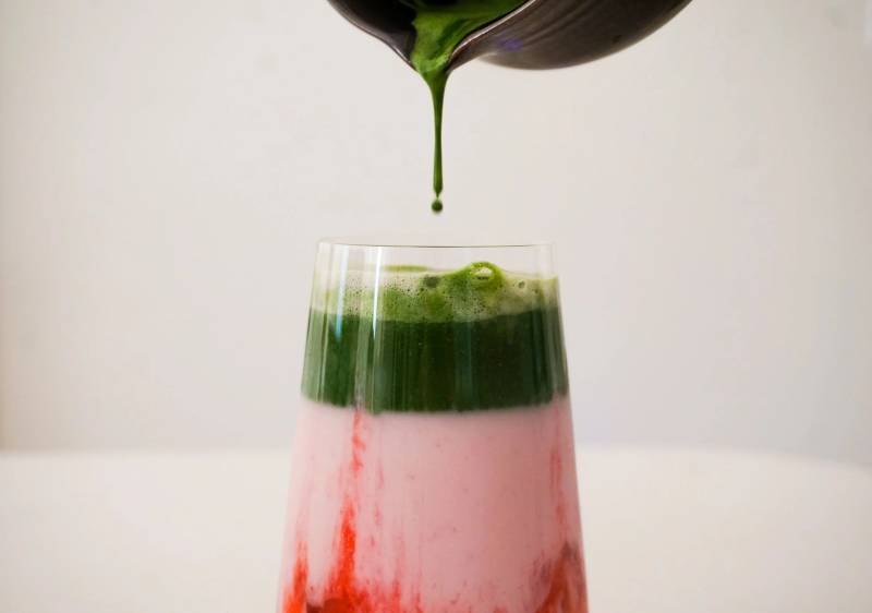 Matcha poured over strawberry milk in a glass